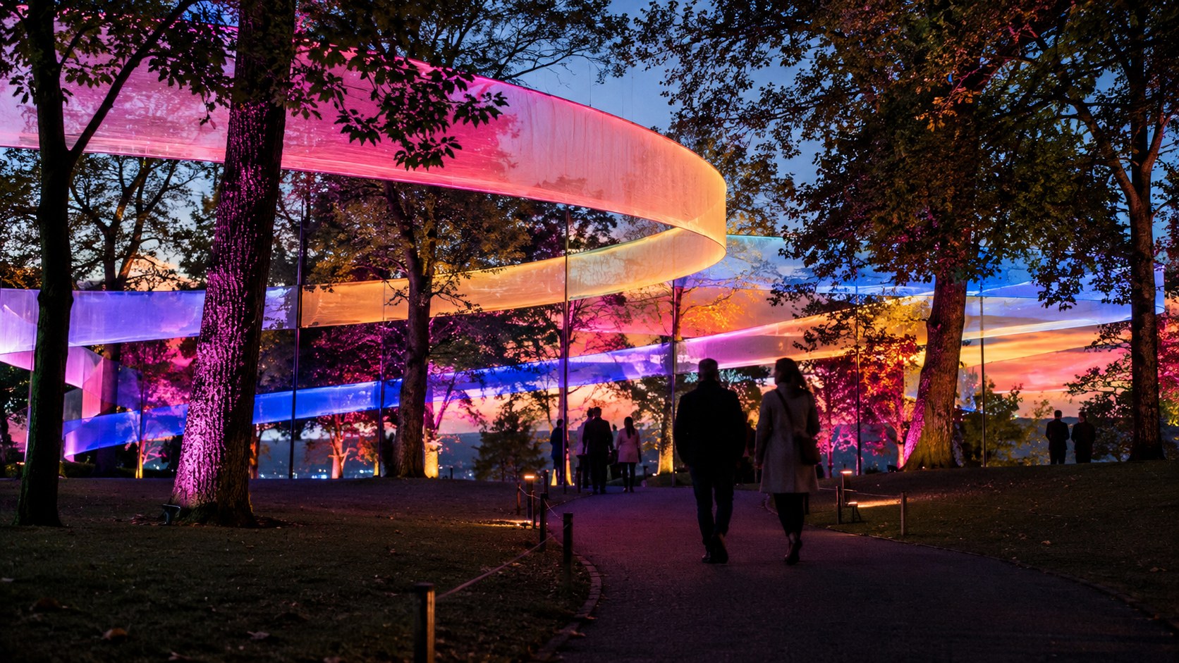 KI-generiertes Symbolbild: Fiktive Lichtinstallation mit leuchtenden Farbbändern und Besuchersilhouetten im Park.