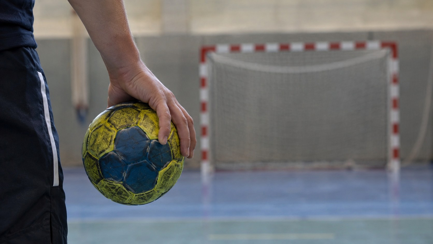 KI-generiertes Symbolbild: Hand mit Handball vor einem Hallentor, ohne erkennbare Spieler.