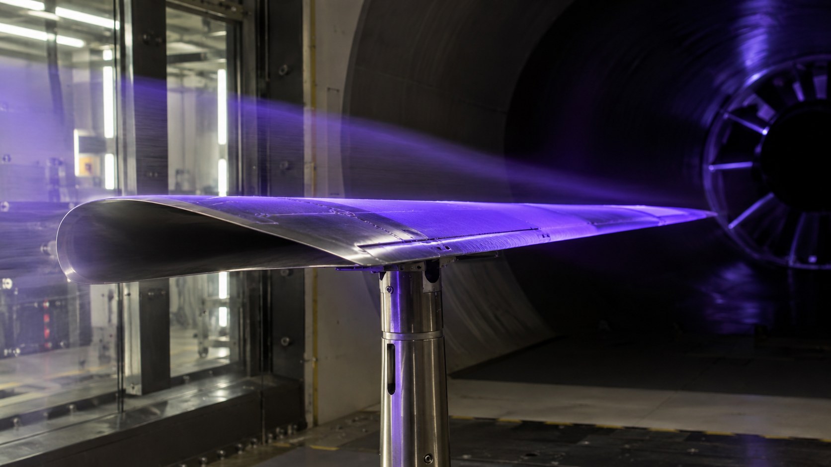 KI-generiertes Symbolbild: Metallischer Modellflügel mit violetter UV-Beleuchtung im Windkanal.