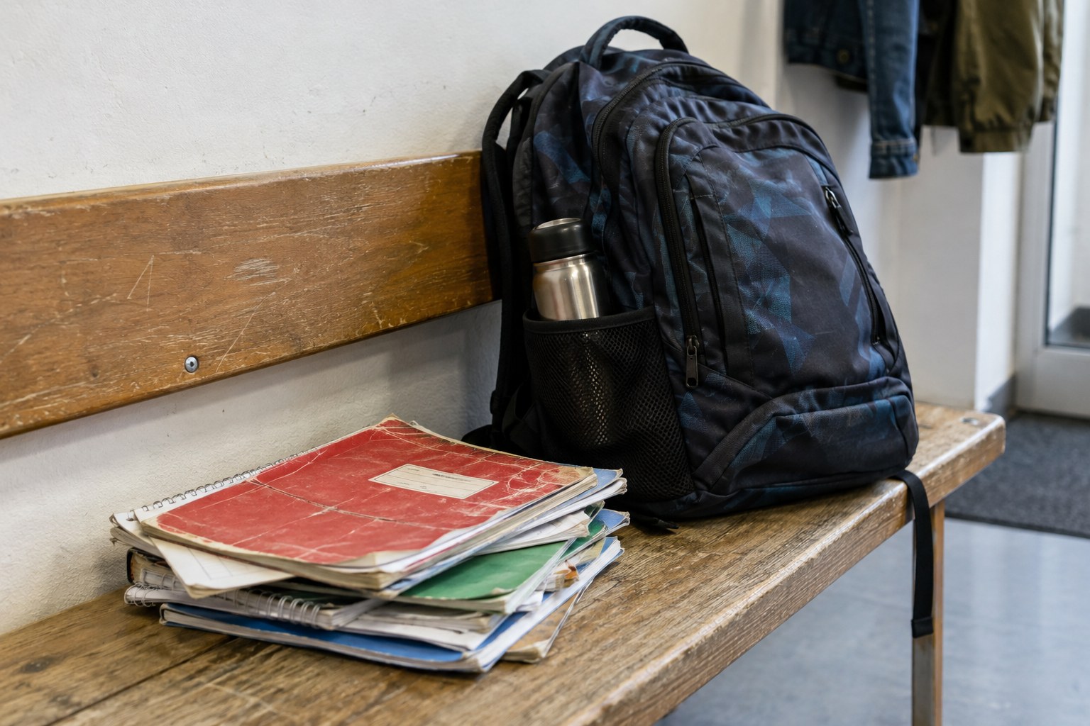 Schultasche und Hefte auf einer Holzbank.