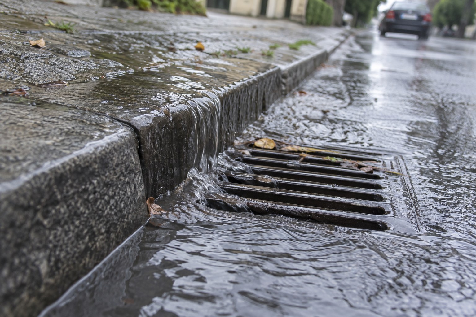 Regenwasser fließt an einem Straßenablauf zusammen.