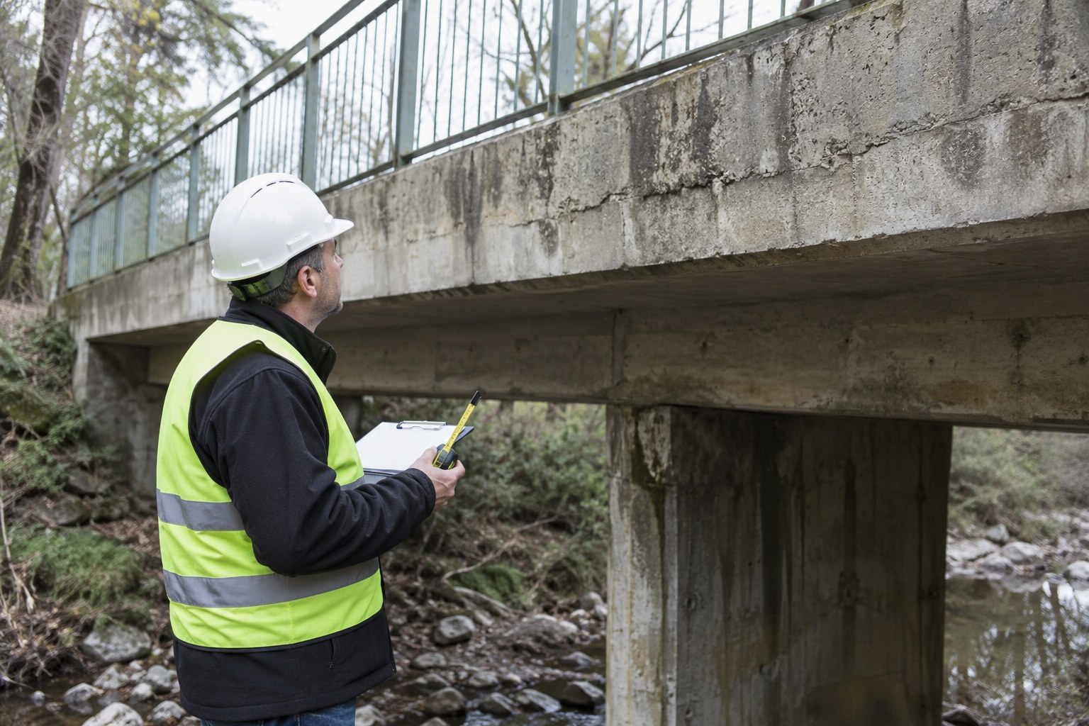Ein Fachmann betrachtet eine Betonbrücke und hält Prüfunterlagen bereit.