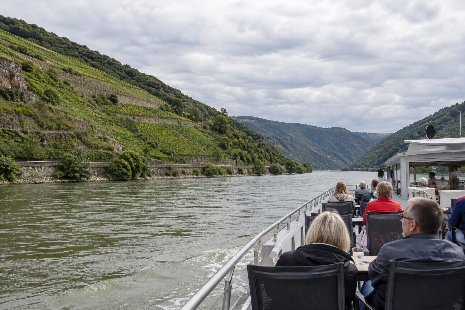 Passagiere fahren auf einem Ausflugsschiff durch ein Flusstal.