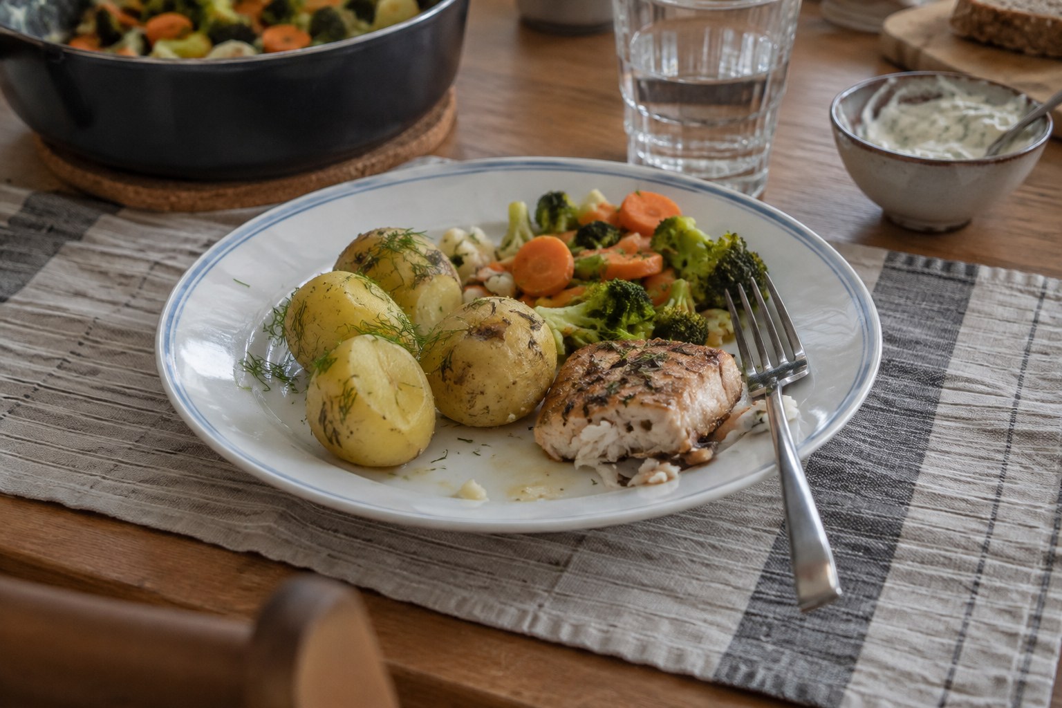 Eine Mahlzeit mit Gemüse, Kartoffeln und Fisch steht auf einem Tisch.