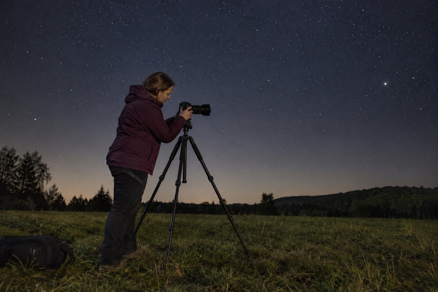 Eine Fotografin richtet nachts eine Kamera auf einem Stativ aus.
