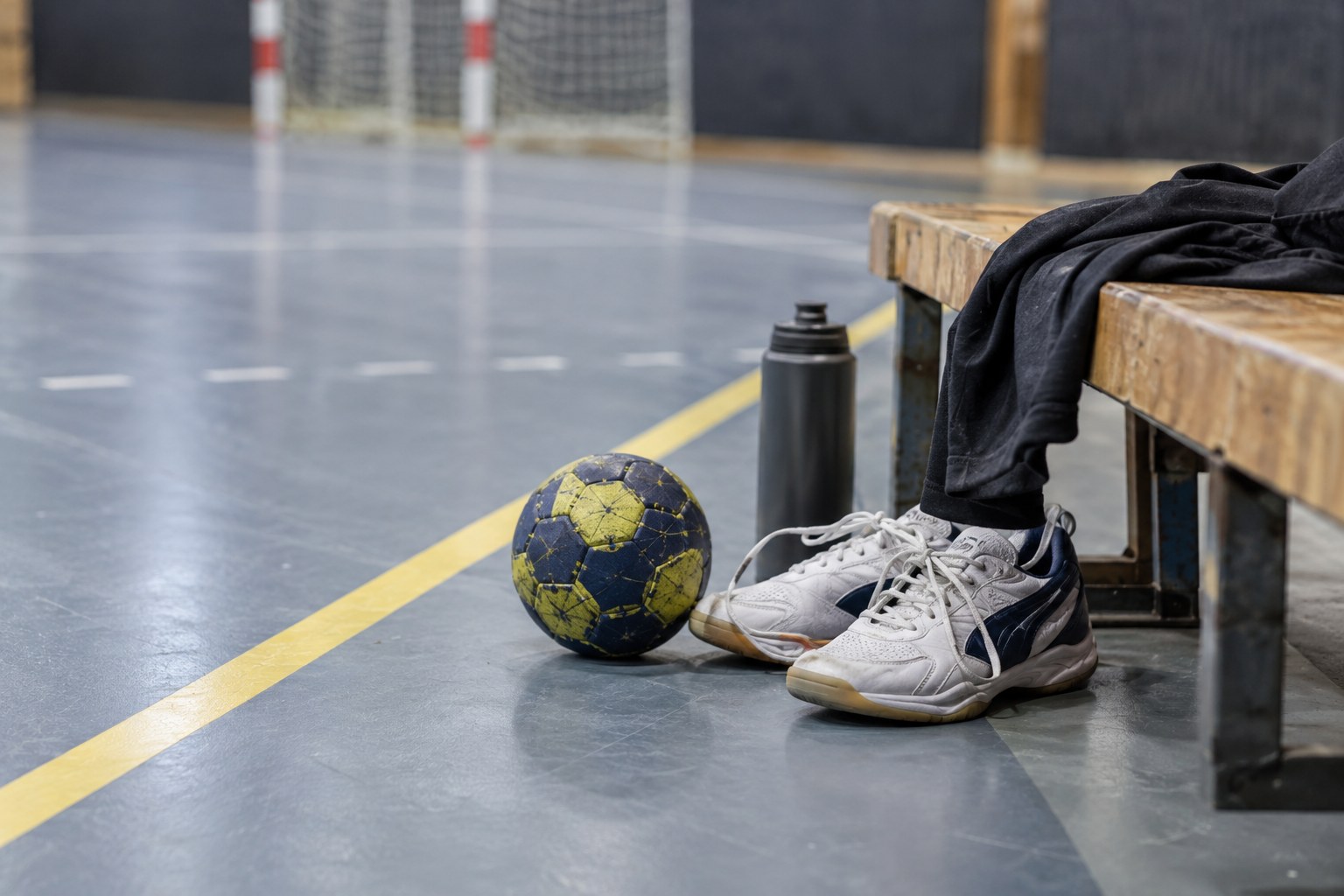 Ein Handball und Sportschuhe liegen neben einer Hallenbank.