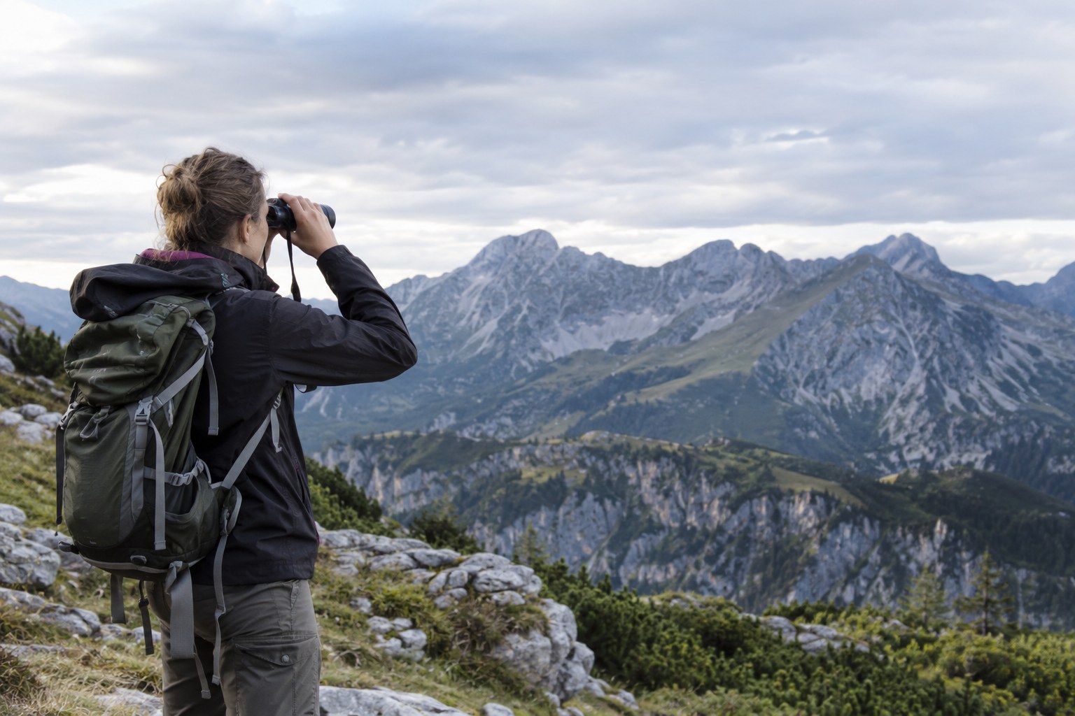 Eine Wildtierforscherin beobachtet einen Berghang mit dem Fernglas.