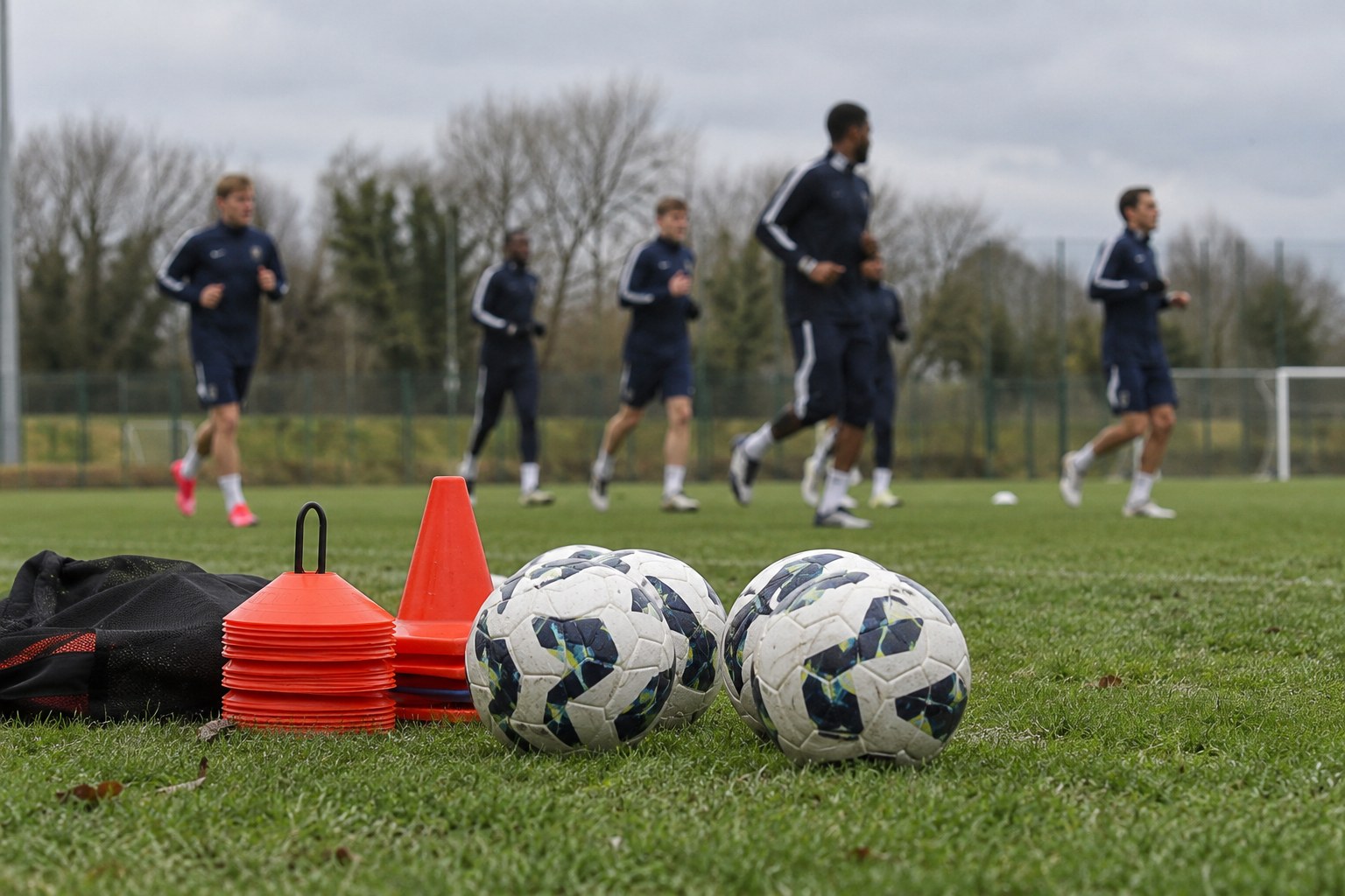Fußbälle und Hütchen am Rand eines Trainingsplatzes.