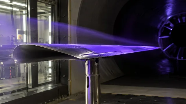 KI-generiertes Symbolbild: Metallischer Modellflügel mit violetter UV-Beleuchtung im Windkanal.