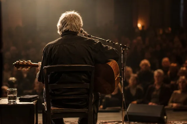 Ein nicht identifizierbarer Musiker mit Akustikgitarre auf einer kleinen Bühne; kein Porträt von Reinhard Mey.