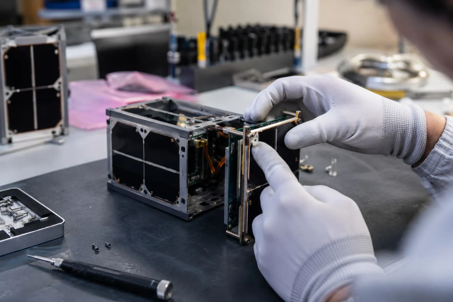 Hände eines Technikers arbeiten an einem kleinen Satelliteninstrument.