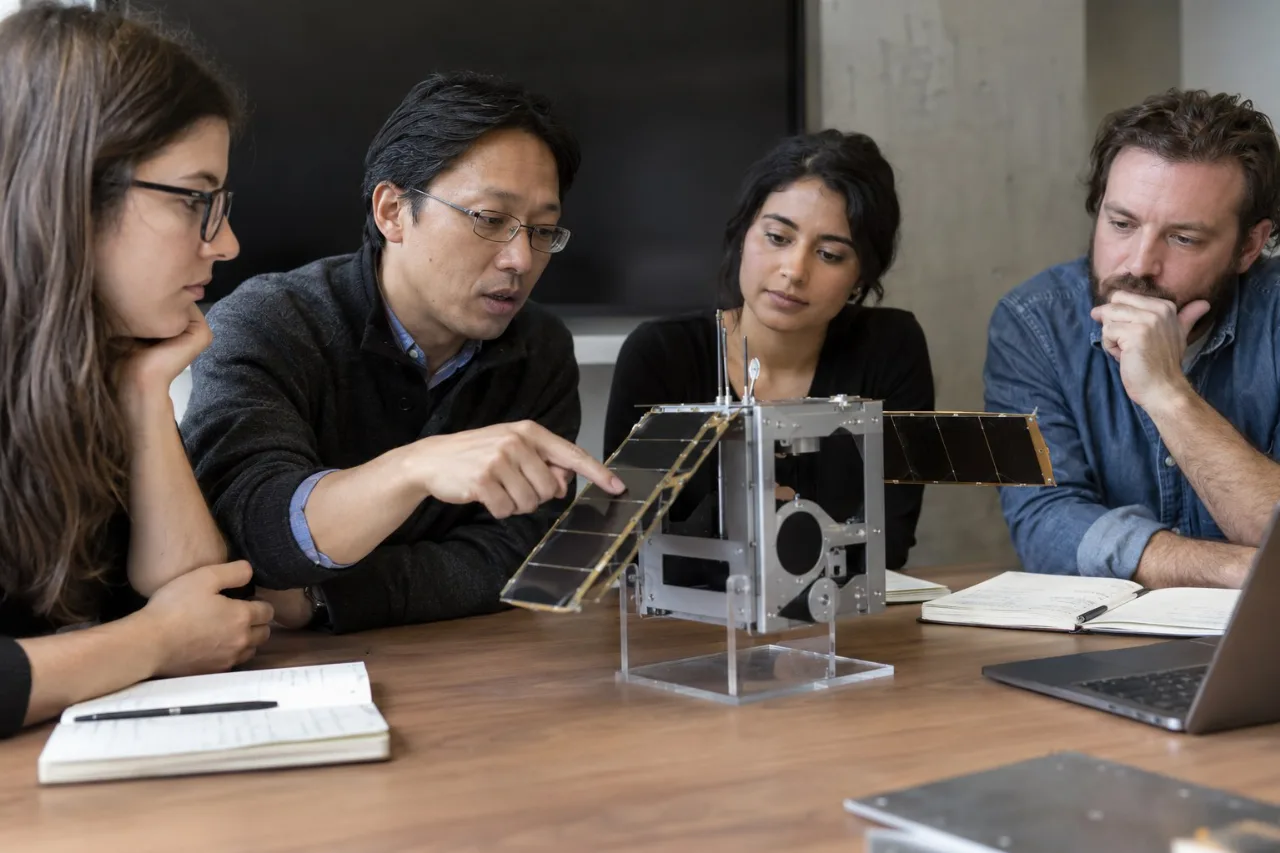 Internationale Forschende diskutieren an einem Tisch über ein Satellitenmodell.